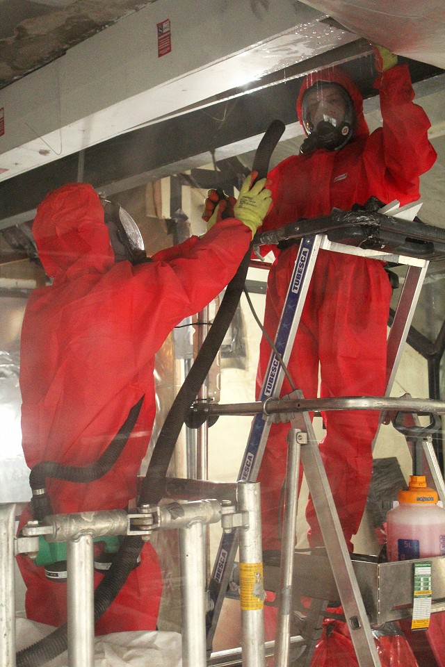 Asbestos operatives inside the enclosure undertaking the shadow vac procedure to remove asbestos debris